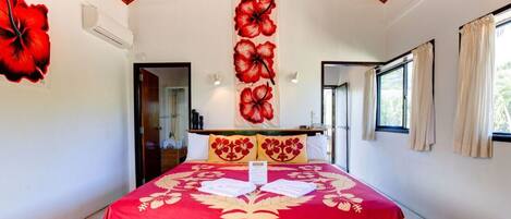 Habitación de hotel con una cama grande, techo de madera, colcha de color rojo y beige, y decoración floral roja en la pared.
