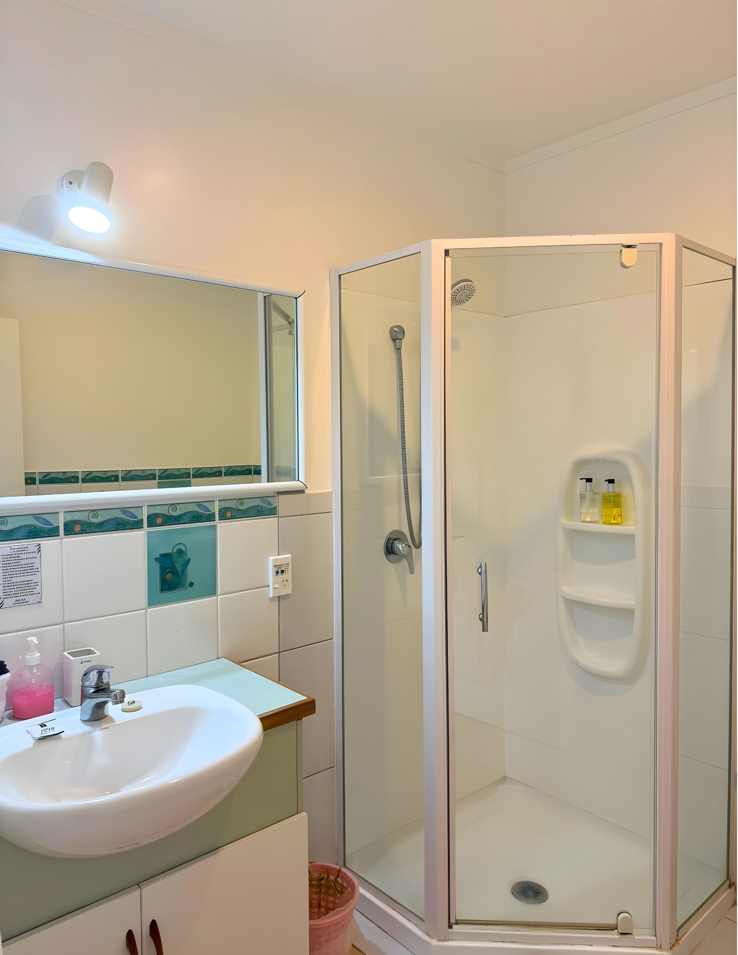 A bathroom with a glass-enclosed shower, a sink with a mirror above it, and a tiled backsplash.