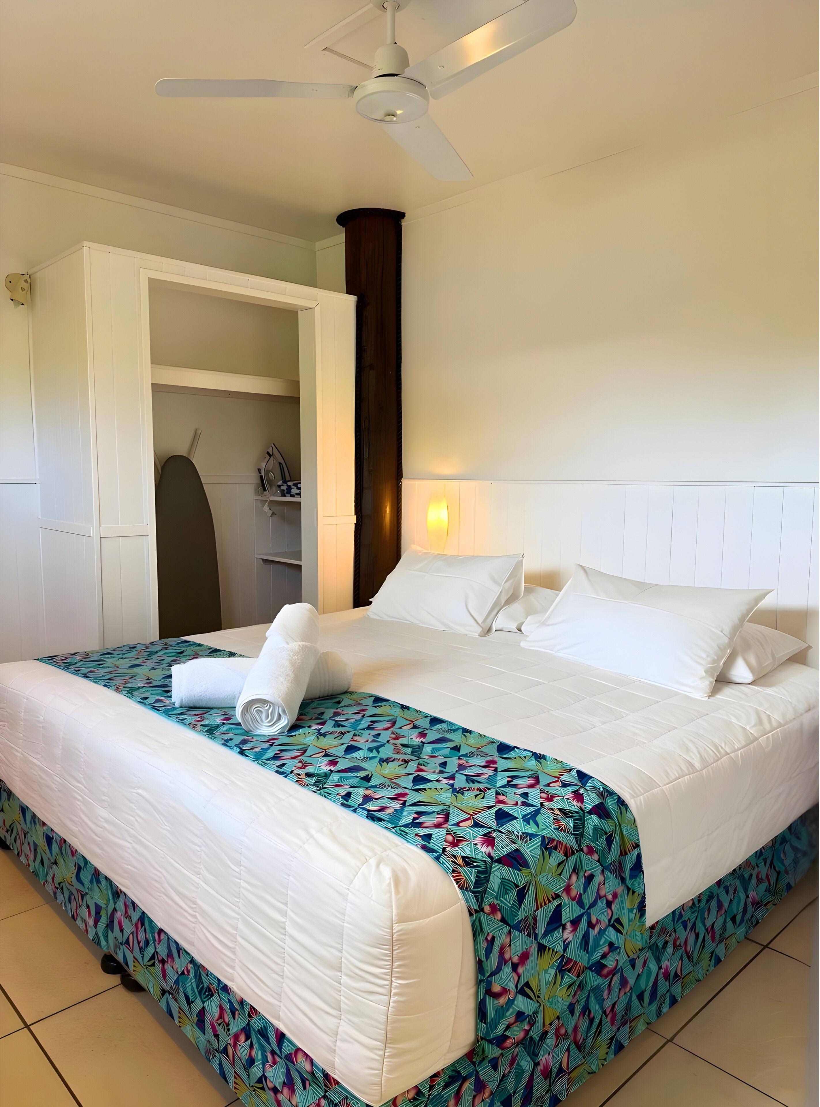 A neatly made bed with white linens and a colorful floral bedspread.