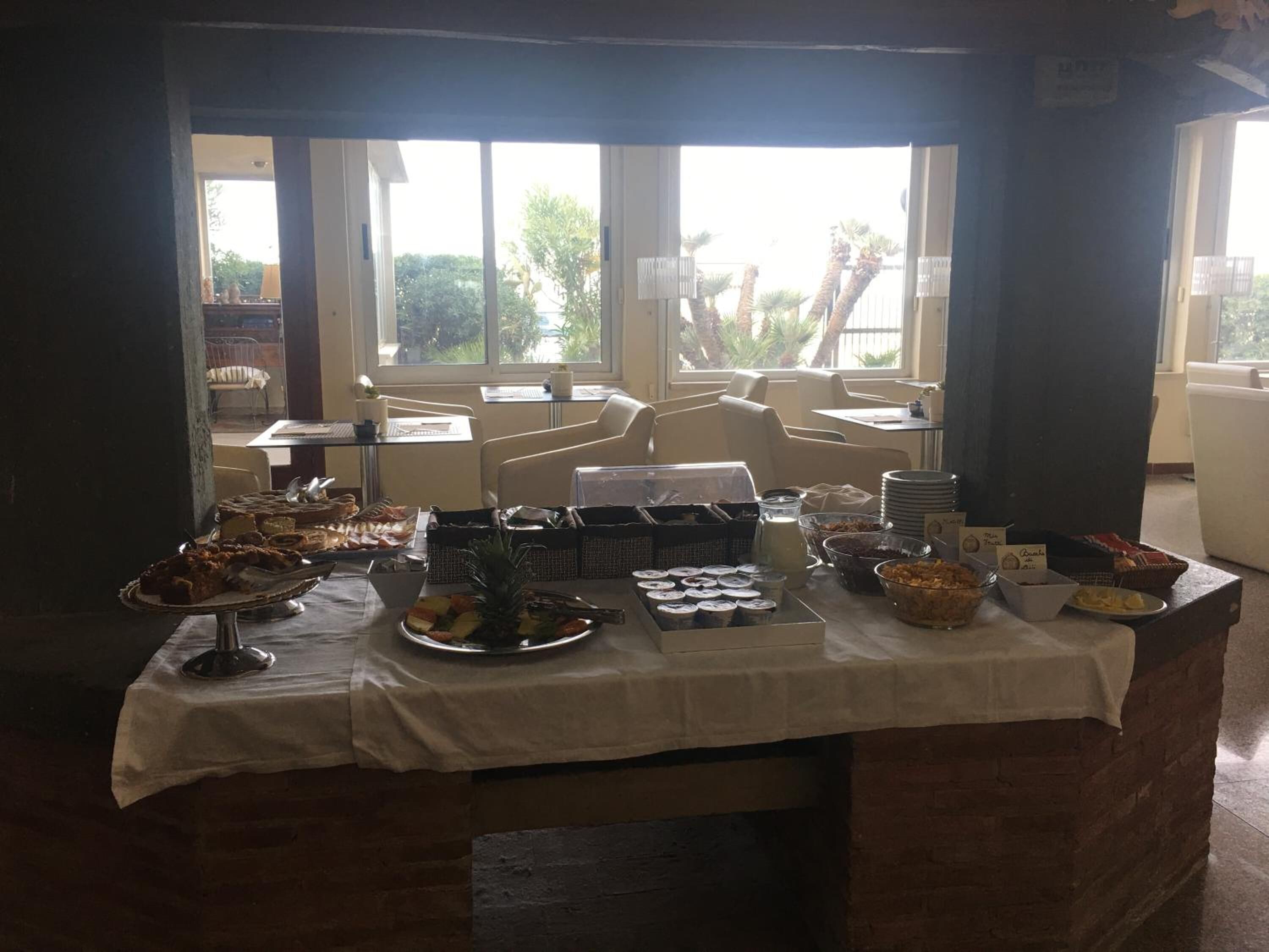 Una mesa de buffet con diversos alimentos y condimentos, con vistas a palmeras a través de ventanas.