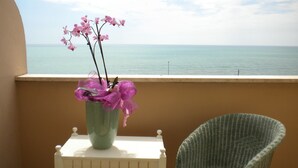 En balkon med havudsigt, en fletstol og en vase med lyserøde blomster.