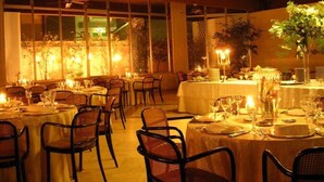 En restaurant med flere borde dækket til spisning, med en hyggelig atmosfære, stearinlys og udsigt til det fri gennem store vinduer.