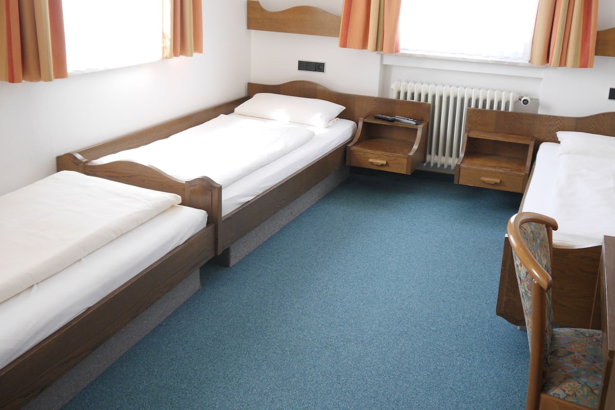 A hotel room with two single beds, a wooden desk with a chair, and a radiator.