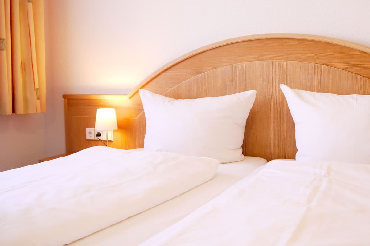 A hotel room with a wooden headboard, two white beds, and a bedside lamp.