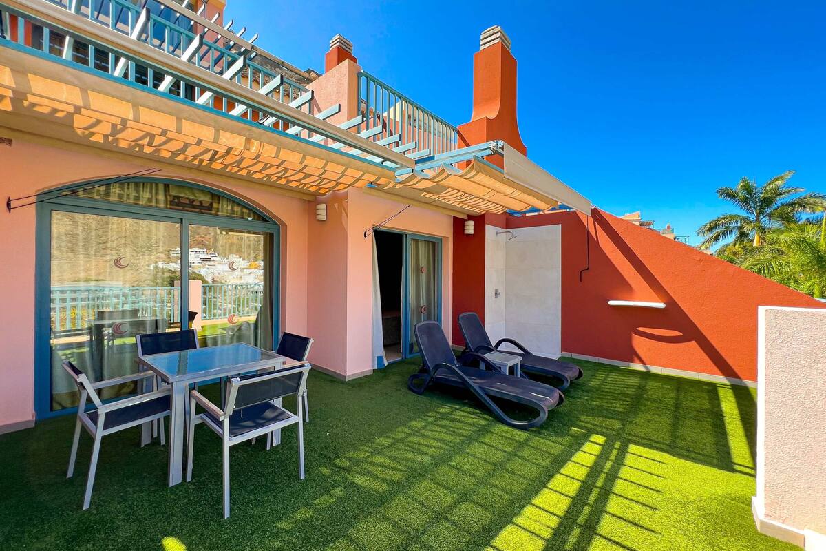 Un balcon avec une porte-fenêtre, une table avec des chaises et un transat.