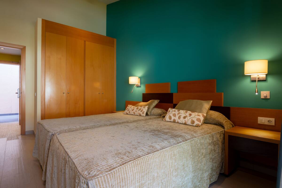 Une chambre à coucher avec un grand lit, deux tables de chevet, une armoire et des lampes fixées au mur.