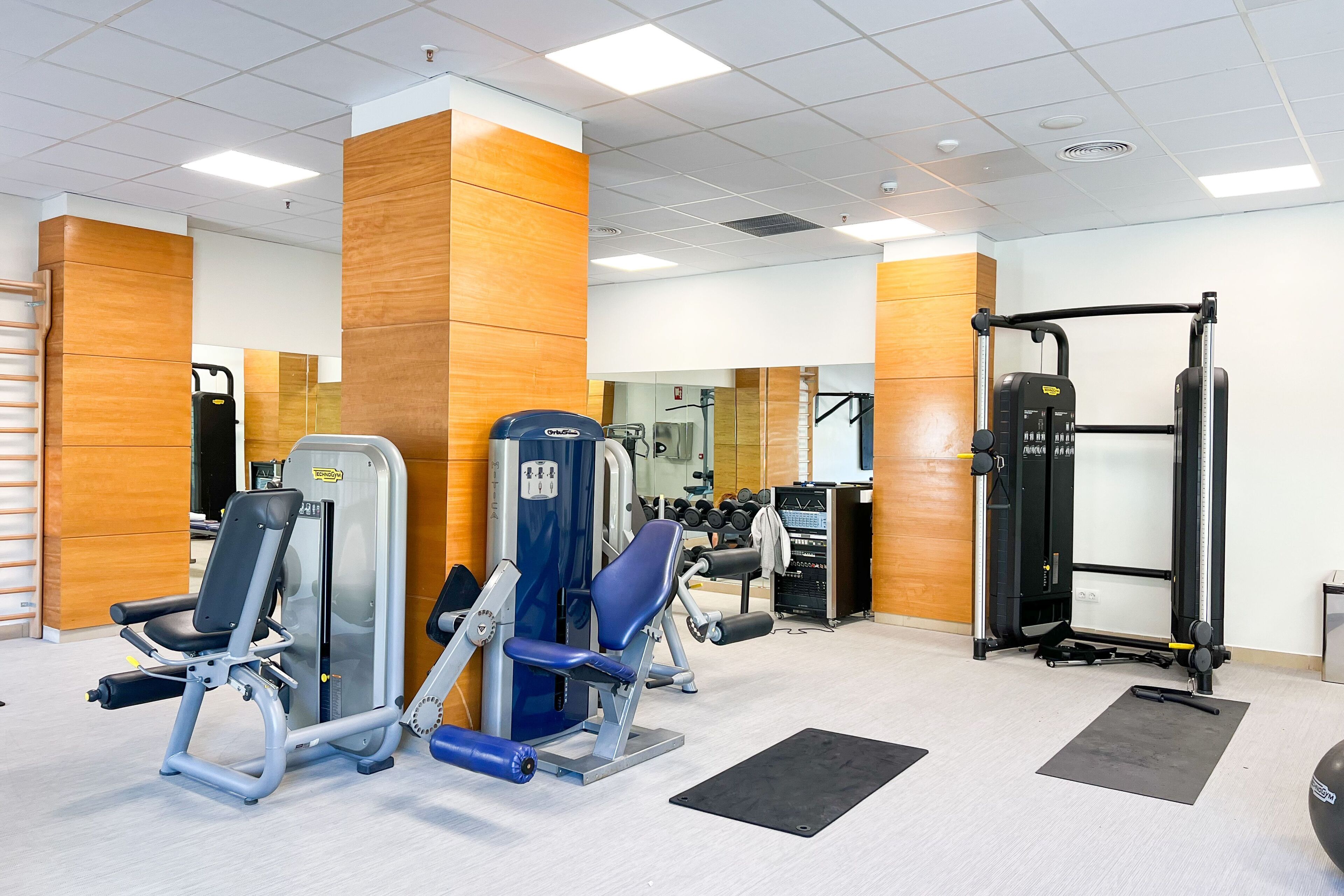A gym with various exercise machines, a mirror, and a rack of dumbbells.