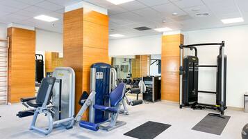 A gym with various exercise machines, a mirror, and a rack of dumbbells.
