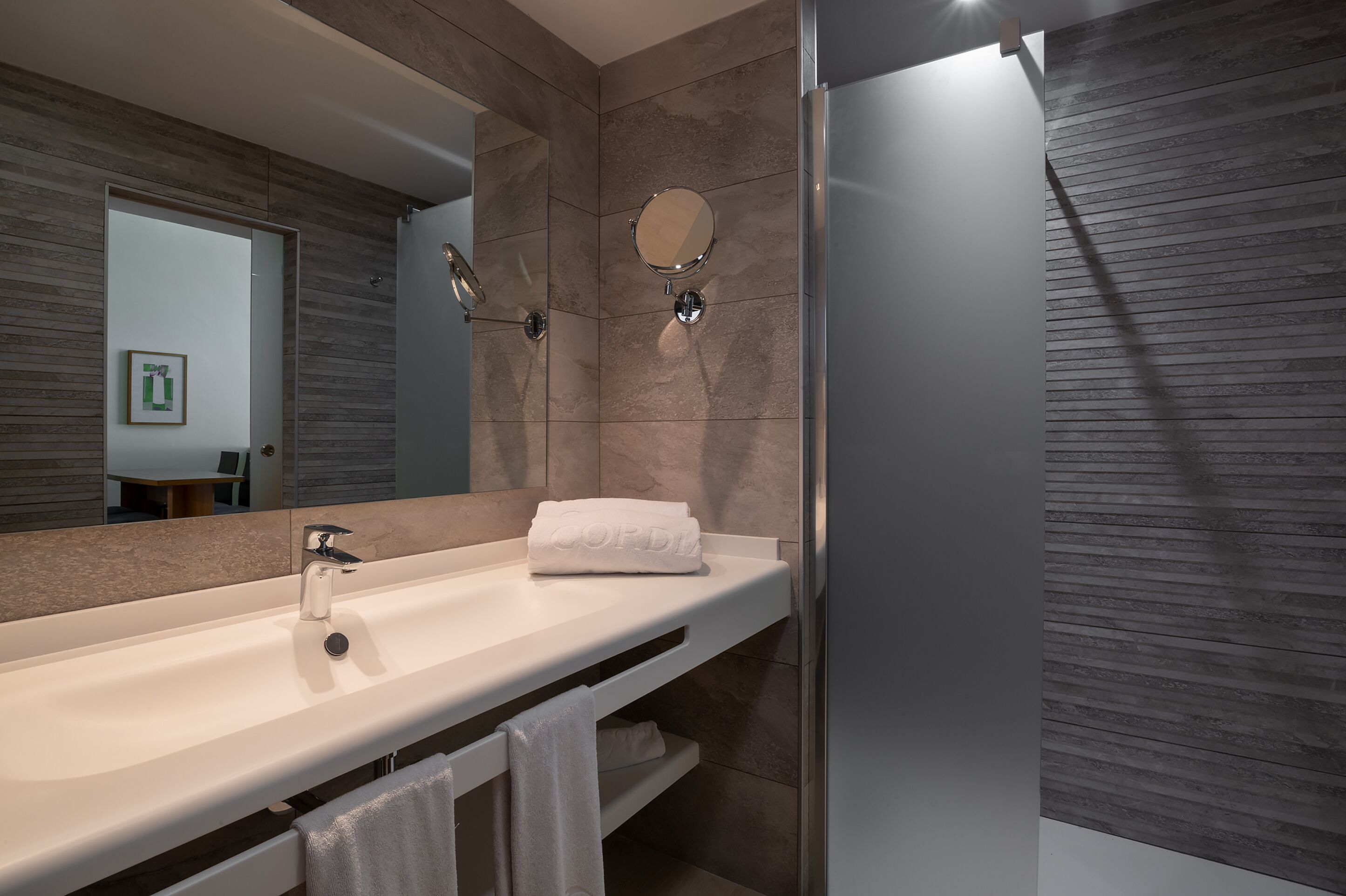 Une salle de bain moderne avec un grand miroir, un lavabo blanc et un porte-serviettes.