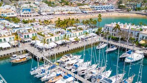 Un puerto deportivo con numerosas embarcaciones amarradas, rodeado de edificios con balcones y palmeras.