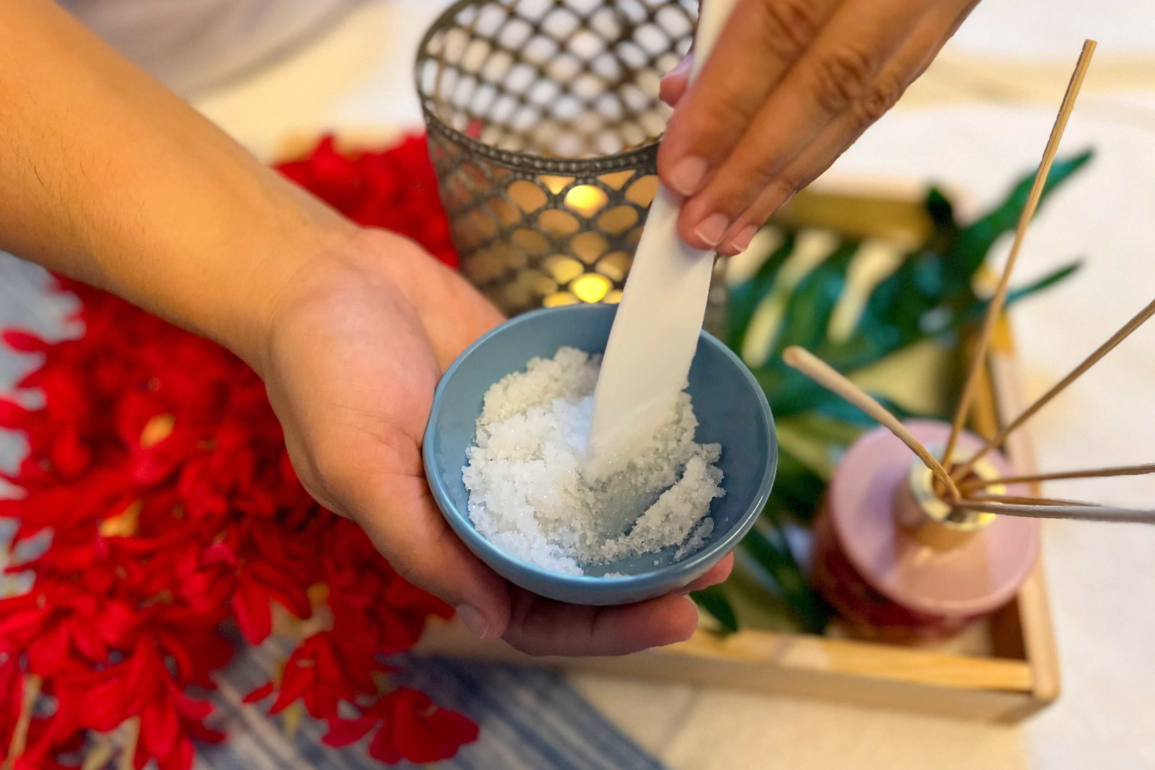 A person holding a bowl of white granular substance, possibly sugar, with a wooden utensil.