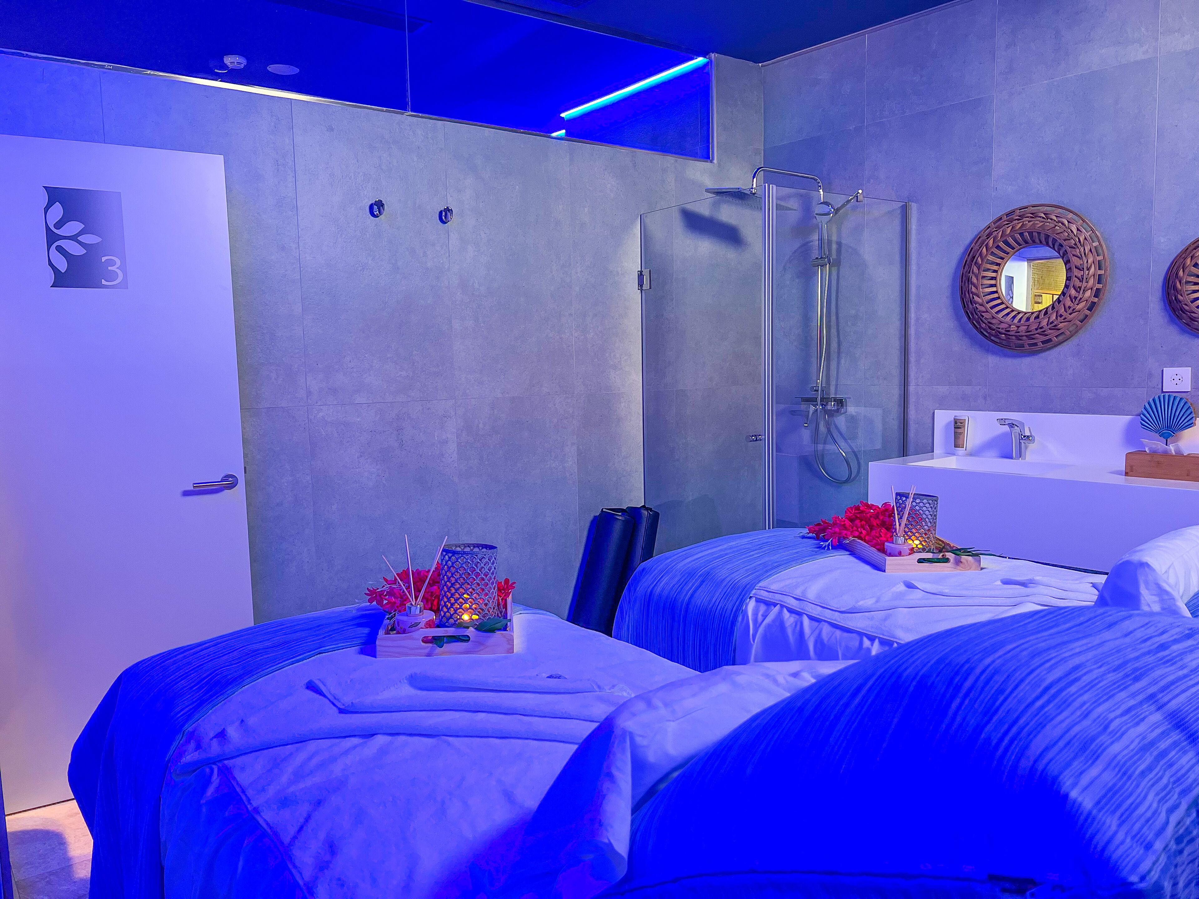 Ein modernes Hotelzimmer mit zwei Betten, einer Dusche und einem Badezimmer mit Waschbecken und Spiegel.