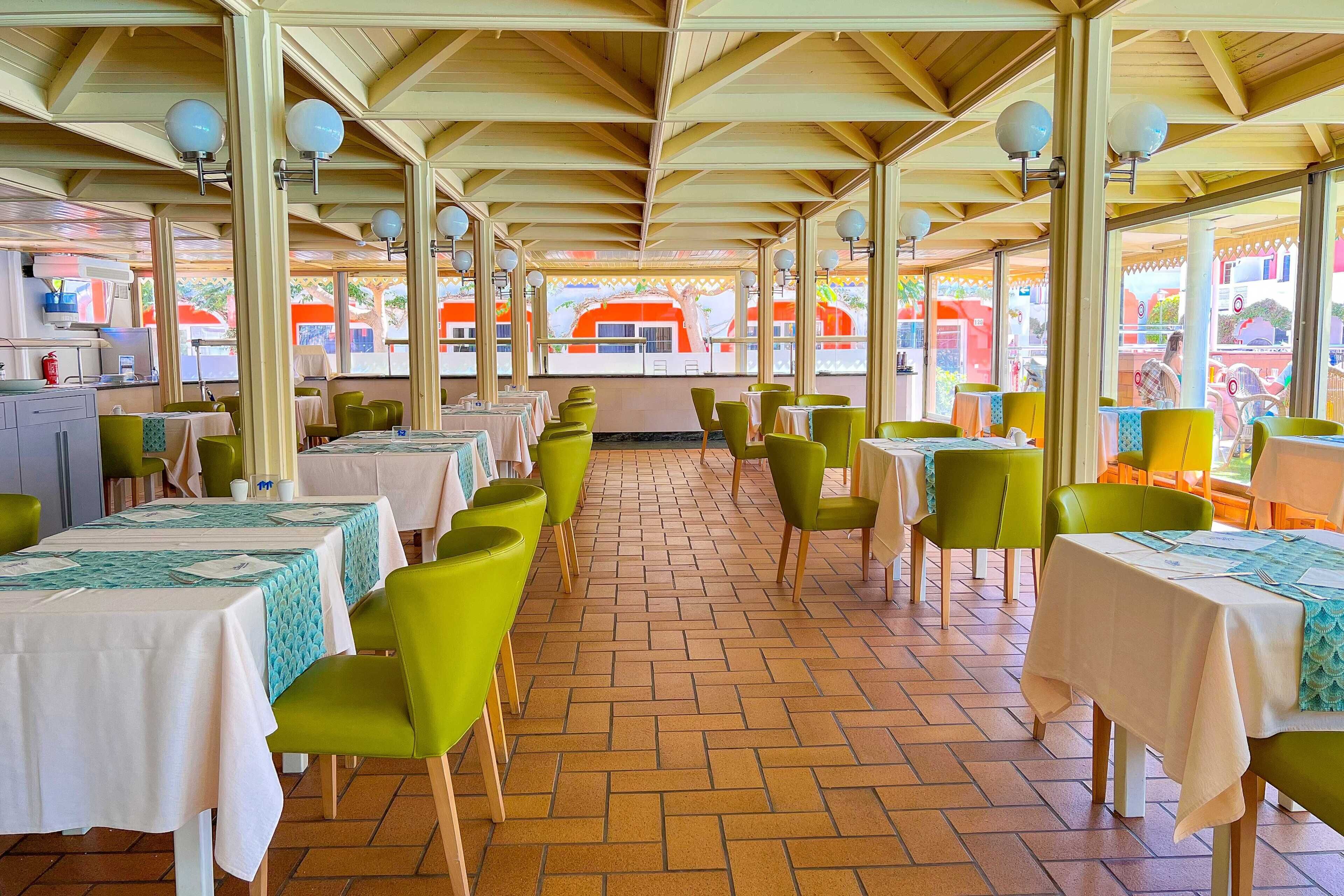 A restaurant with outdoor seating, green chairs, and tables covered with white tablecloths.