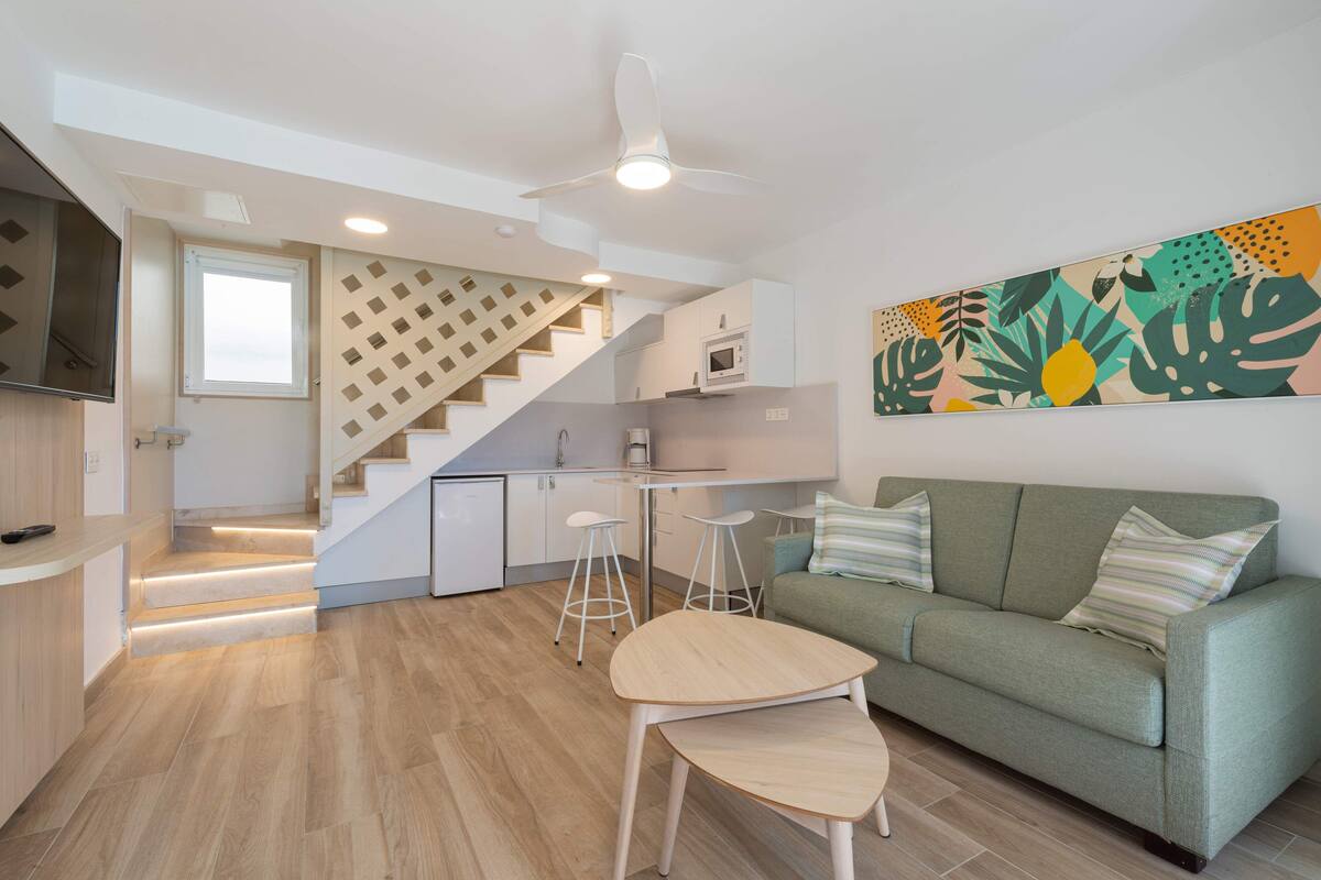 Um espaço de estar moderno com uma escada que leva a uma cozinha, um sofá verde e uma mesa com banquetas.