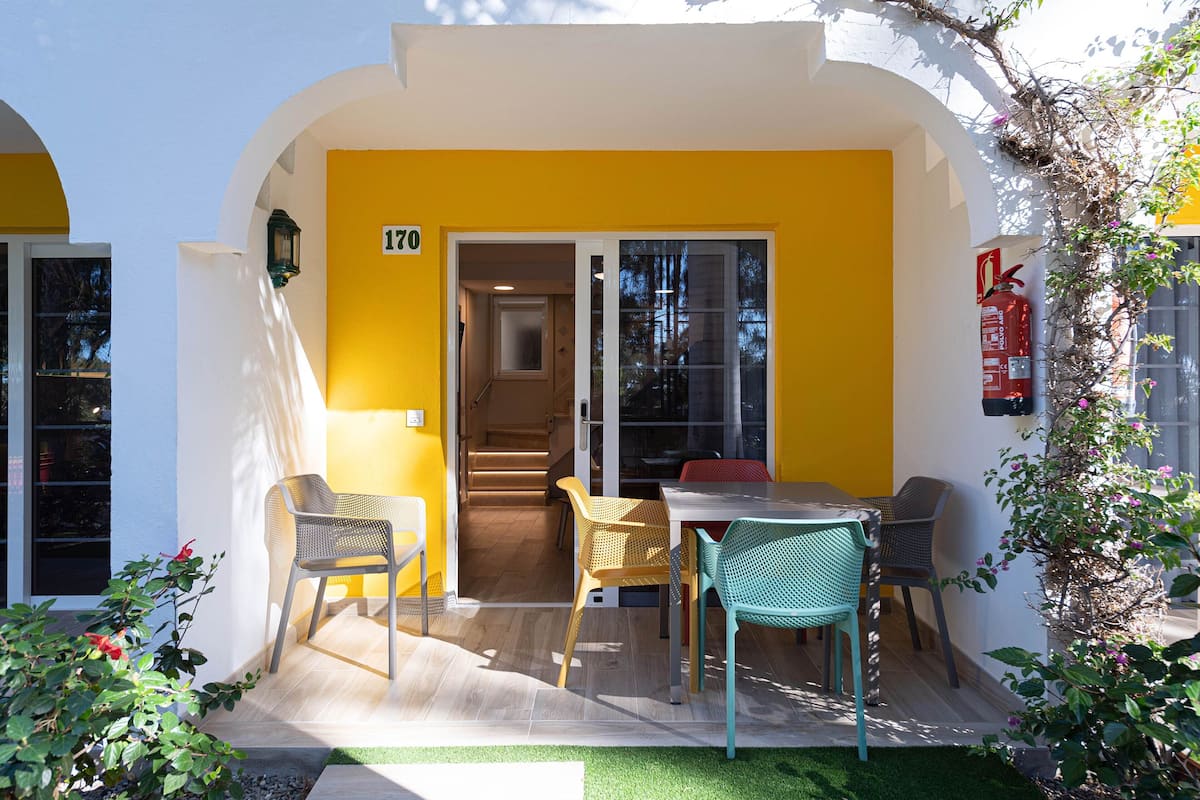 Um edifício amarelo com uma placa indicando o número 170, um extintor de incêndio e um pátio com cadeiras e uma mesa.