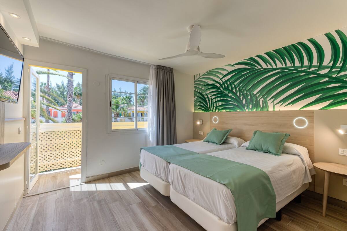 Quarto de hotel moderno com duas camas, uma janela grande e vista para o exterior.