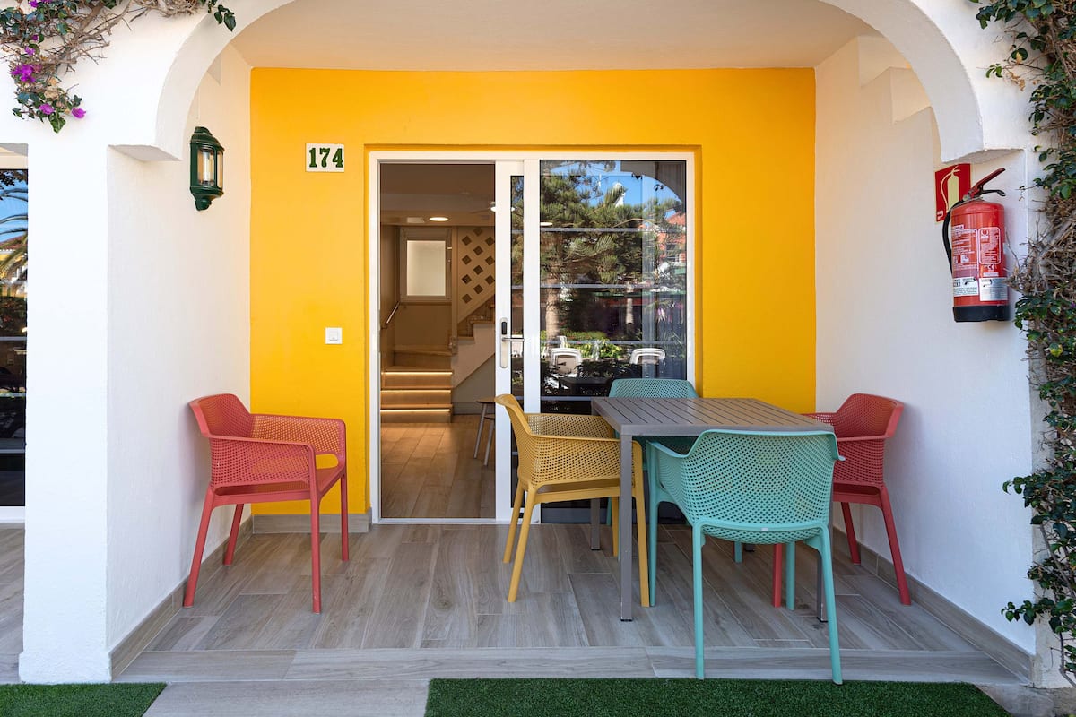 Um pátio externo com parede amarela, uma mesa e quatro cadeiras.