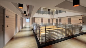 A modern hotel corridor with a central glass railing, multiple doors, and overhead lighting.