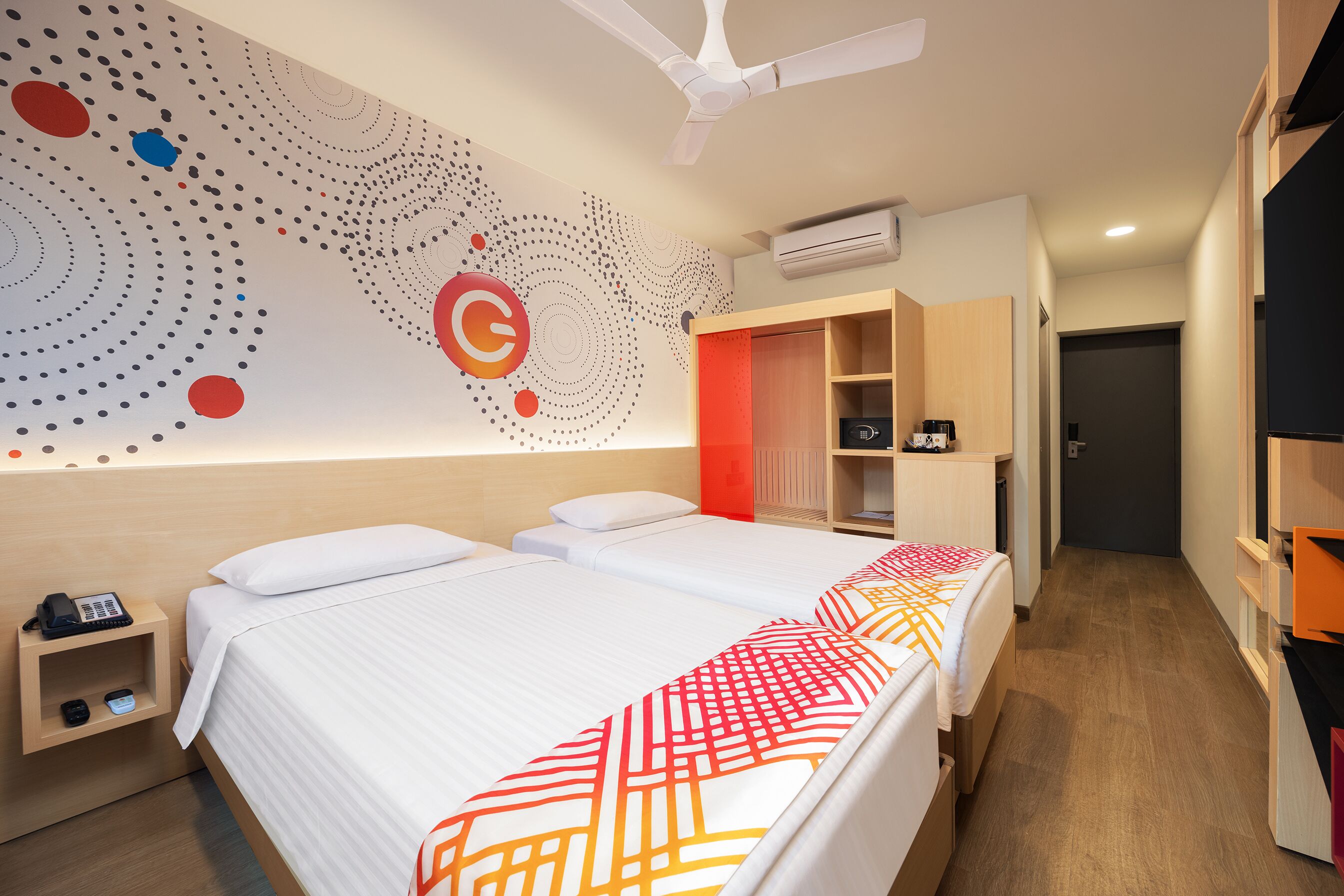 Habitación de hotel con dos camas, un escritorio con teléfono, un armario y una pared con diseño geométrico.