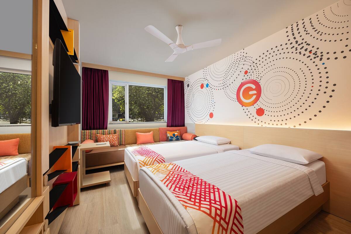 A modern hotel room with two beds, a TV, a ceiling fan, and a large window with curtains.