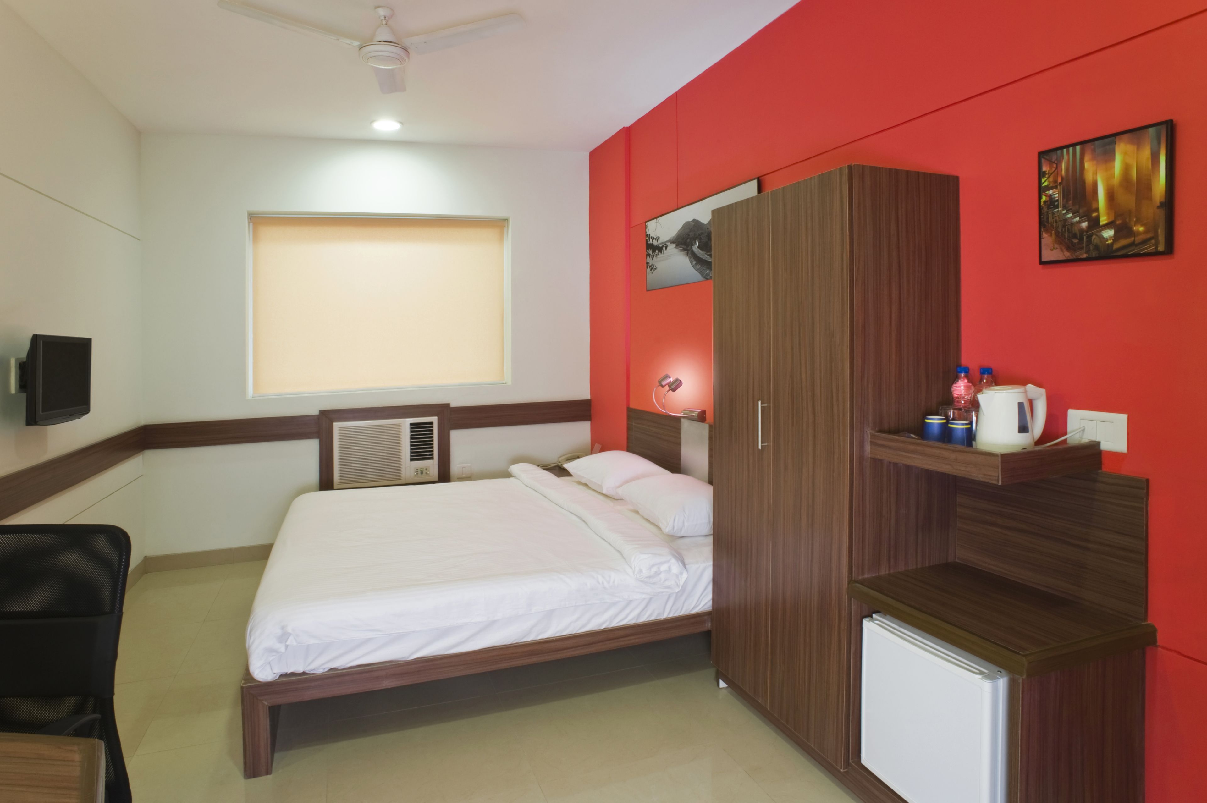 Un dormitorio con cama, armario, escritorio, silla, ventana con persianas, ventilador de techo y televisor de pared.