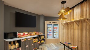 A modern snack bar with a flat-screen TV, snack dispensers, and a refrigerated display.