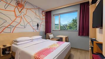 A hotel room with a large bed, a desk, a chair, a TV, and a window with curtains.
