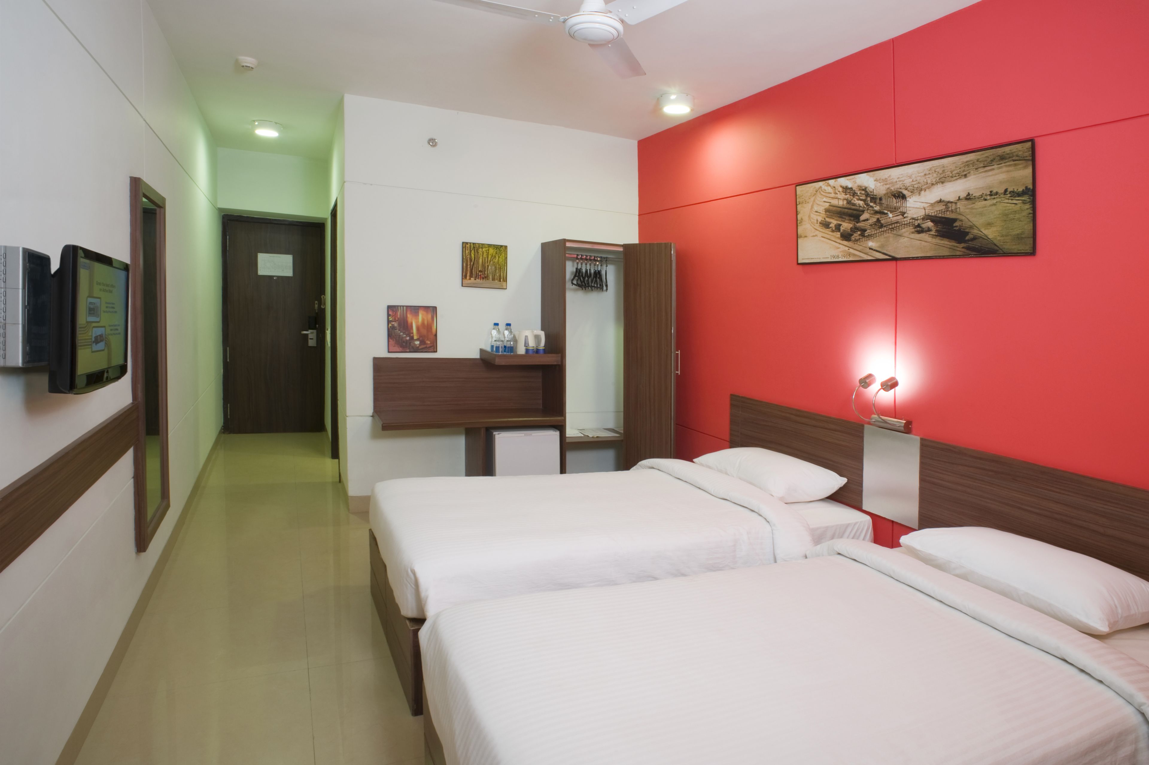 A hotel room with two beds, a desk with a chair, a wardrobe, a television, and a painting on the wall.