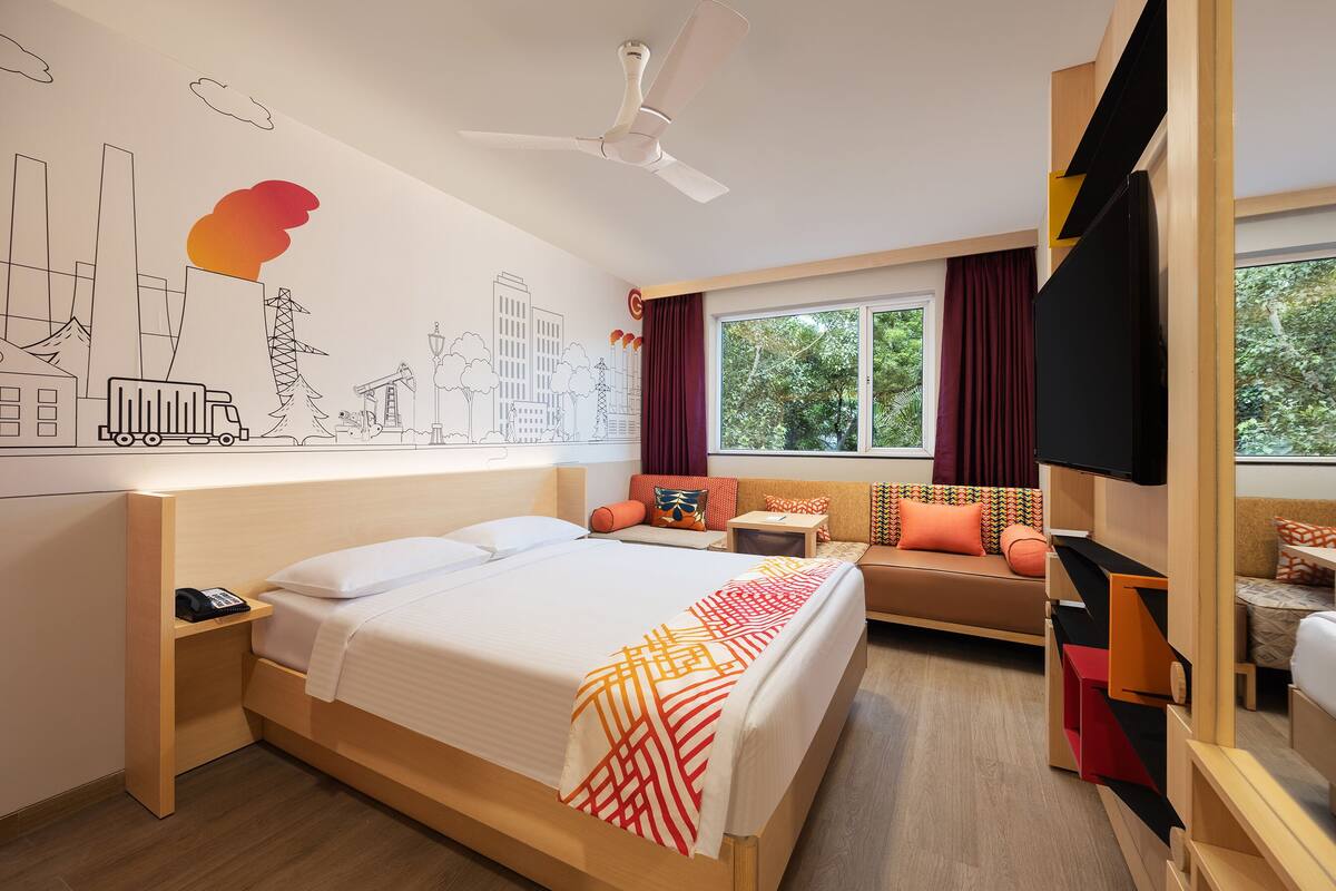 A modern hotel room with a large bed, a desk, a sofa, and a TV.