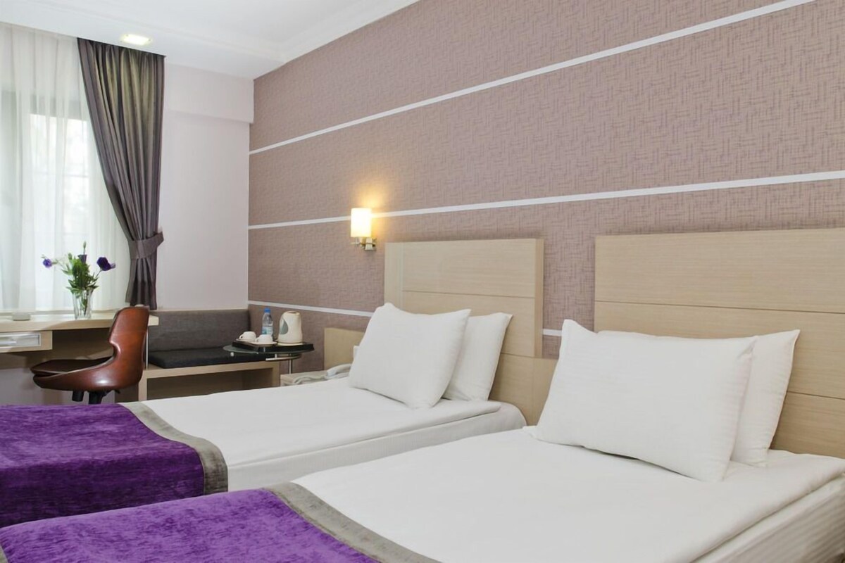 Une chambre d’hôtel avec deux lits, un bureau, une chaise et une lampe fixée au mur.