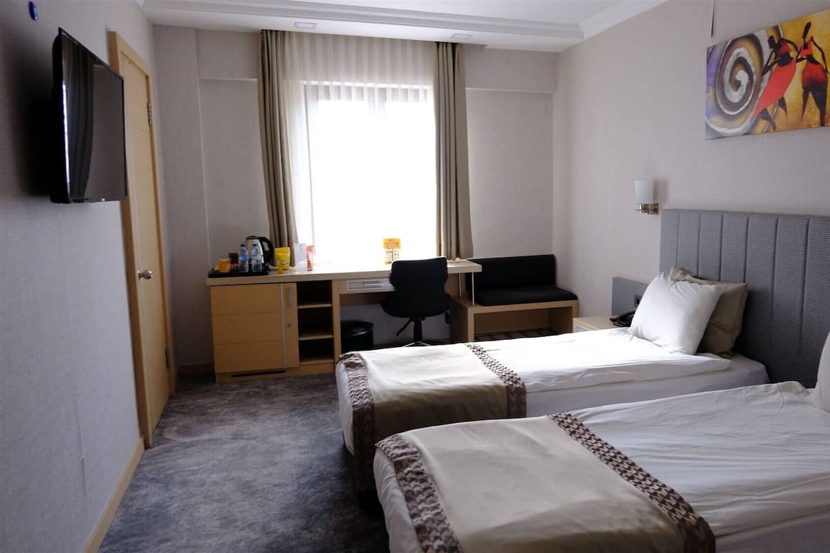 A hotel room with two beds, a desk, a chair, a television, and a painting on the wall.