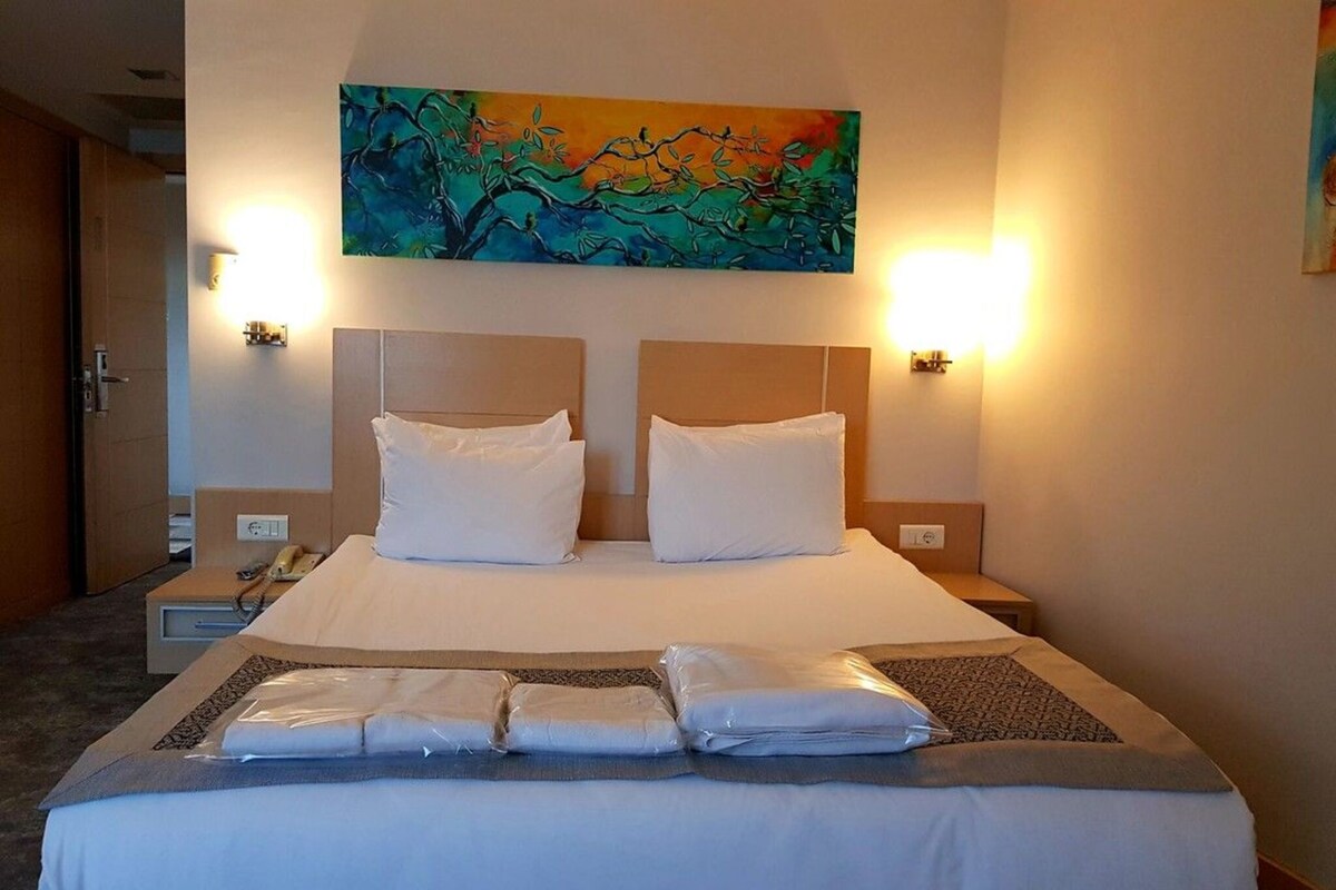 Une chambre d’hôtel avec un grand lit, deux lampes de chevet, un tableau au-dessus du lit et un téléphone sur la table de chevet.