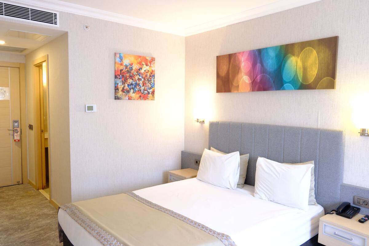 Une chambre d’hôtel avec un lit, une table de chevet, un téléphone et deux tableaux au mur.