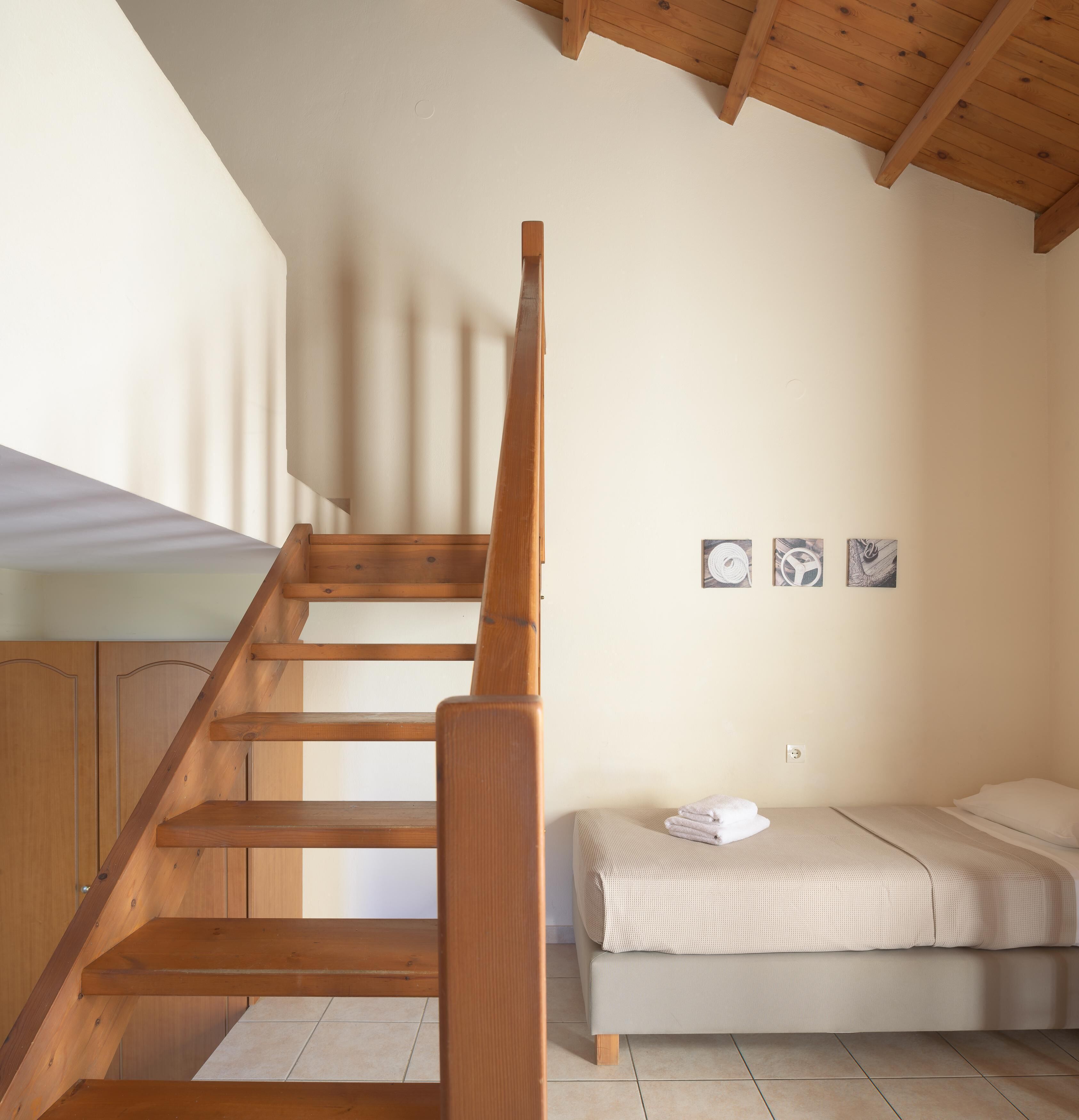A bedroom with a wooden staircase, a bed with a beige blanket, and two framed pictures on the wall.
