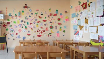 Un aula con pupitres y sillas de madera, paredes decoradas con trabajos infantiles y material educativo.