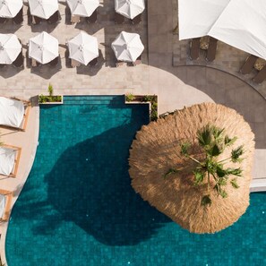 An aerial view of a swimming pool with surrounding lounge chairs and umbrellas, a thatched umbrella, and potted plants. - Asterias Village Resort (Hersonissos)