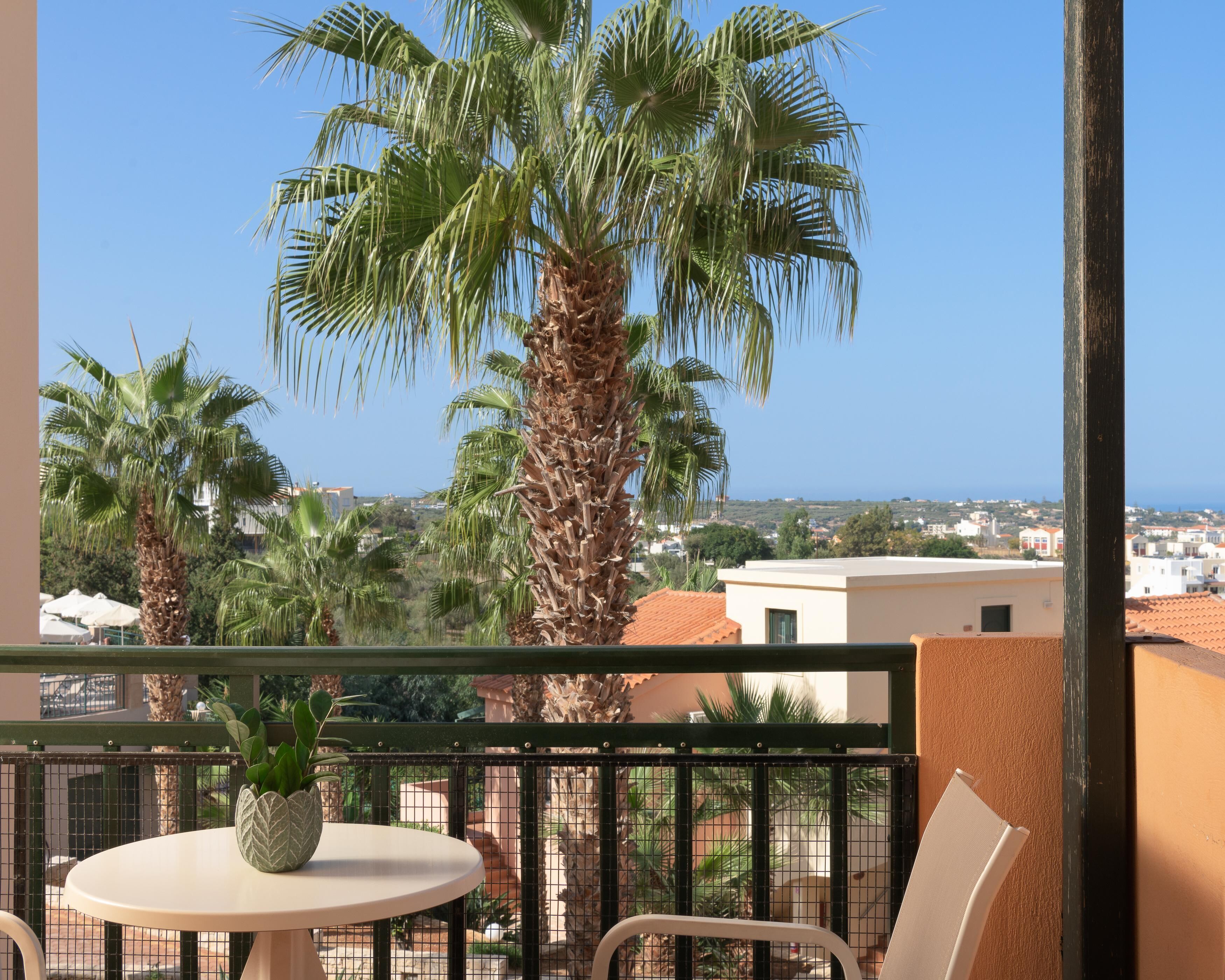 A balcony with a table and chairs, a potted plant, and a view of palm trees and buildings.