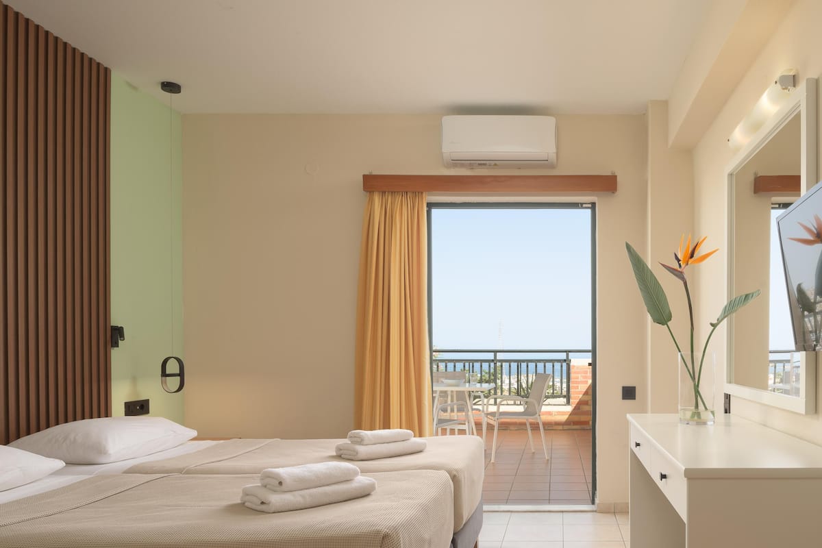 Een hotelkamer met twee bedden, een balkon met een tafel en stoelen, en een airconditioning.
