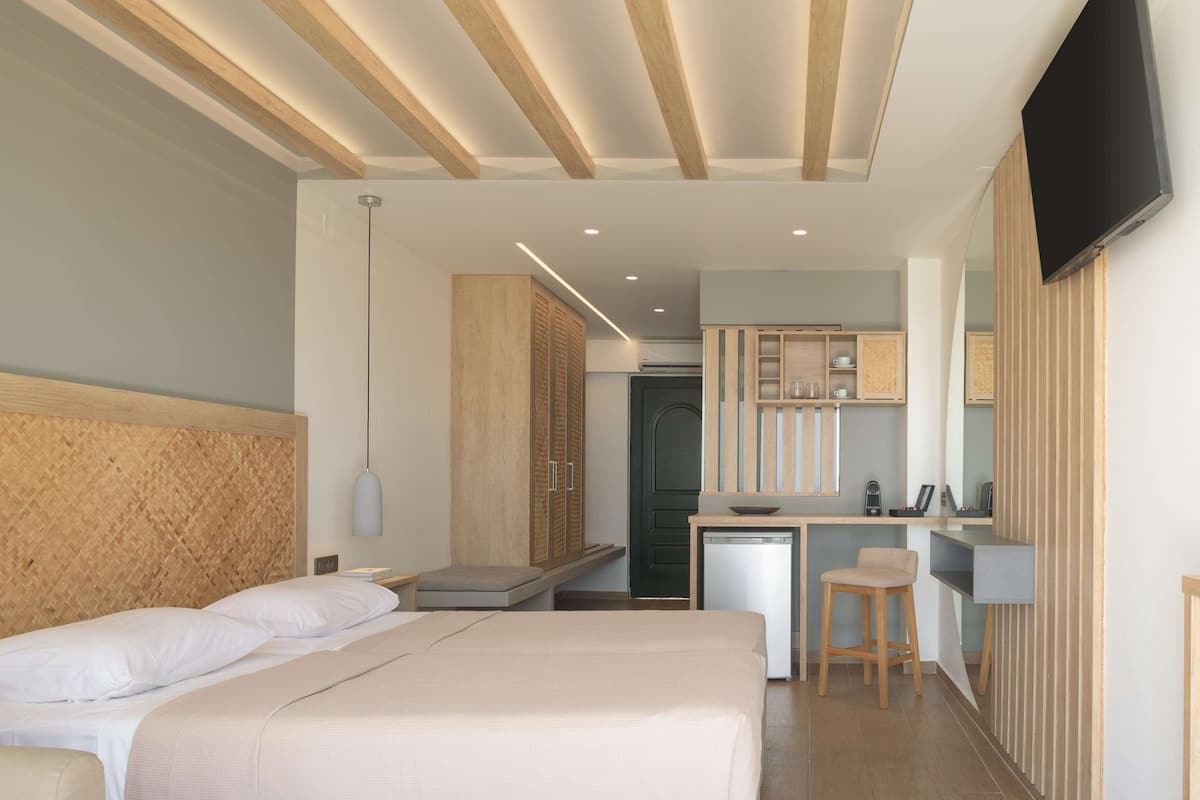 Een moderne hotelkamer met een groot bed, een kleine kitchenette en een aan de muur bevestigde televisie.