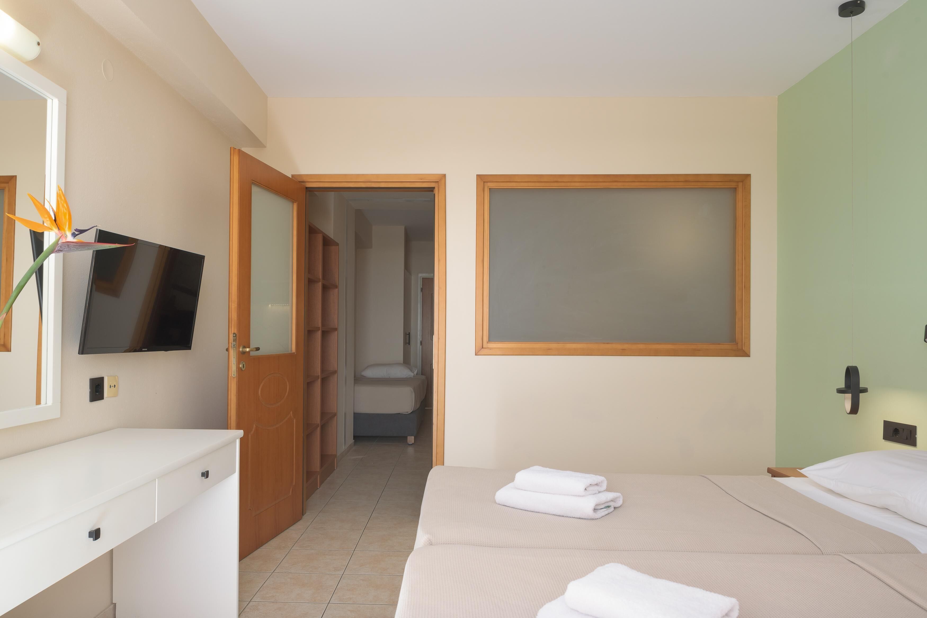 A hotel room with a bed, a TV, a desk, and a bathroom visible through an open door.