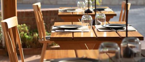 A restaurant with wooden tables and chairs, clear glassware, and a stone wall in the background.