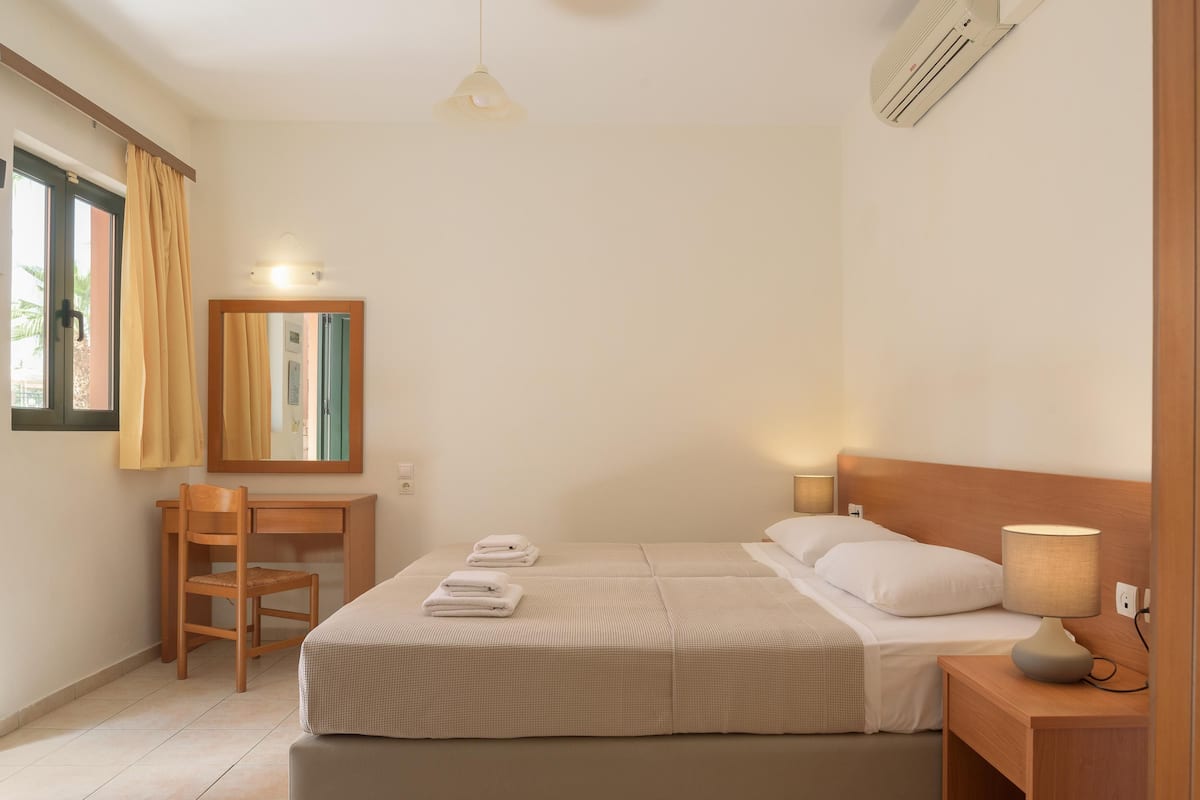 Een hotelkamer met een bed, een bureau, een stoel, een lamp en een raam met gordijnen.
