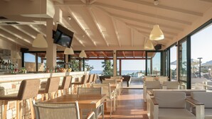 Zona de bar con asientos, un televisor y vista al mar.