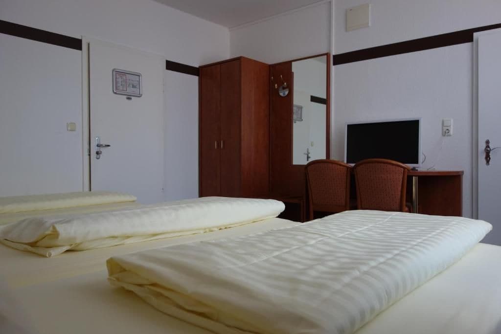 A hotel room with a bed, a desk with a computer, a wardrobe, and a mirror.