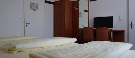 A hotel room with a bed, a desk with a computer, a wardrobe, and a mirror.