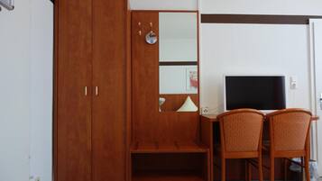 A room with a wooden wardrobe, a desk with a television, and two chairs.