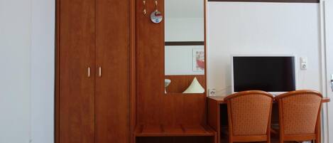 Una habitación con un armario de madera, un escritorio con televisor y dos sillas.