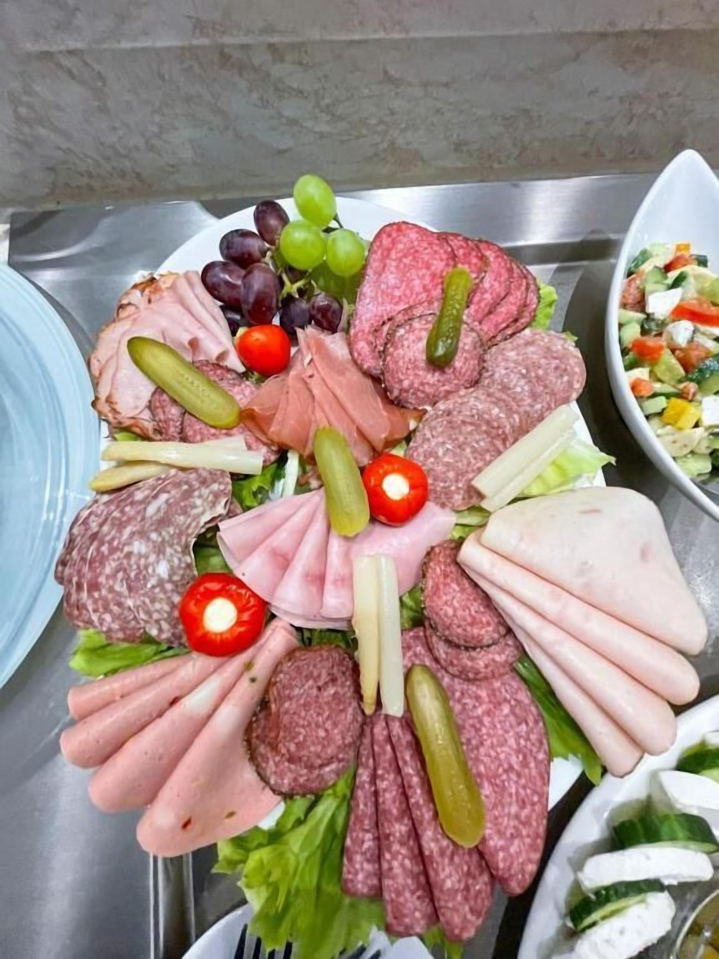 A charcuterie board with various meats, grapes, and pickles.