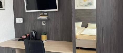 A modern room with a desk, chair, TV, and a bed with a headboard.