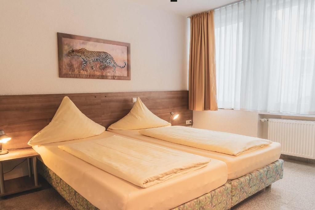 A hotel room with two beds, a headboard, a nightstand, a lamp, a window with curtains, and a leopard painting on the wall.